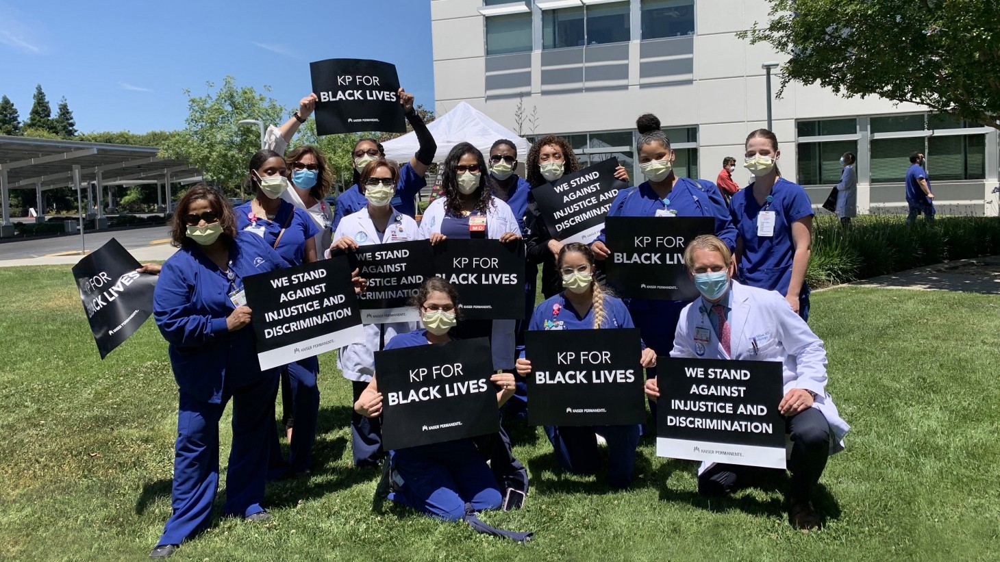A group of health care workers, wearing scrubs and masks, holding signs that read, "KP for Black Lives"