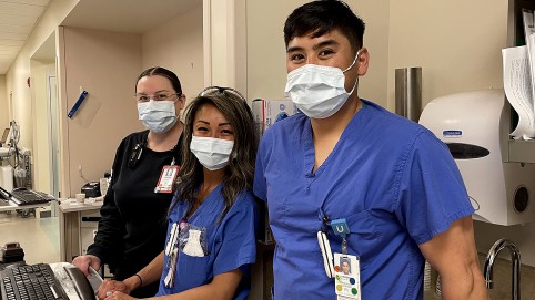 Three health care workers, wearing masks, looking at the camera