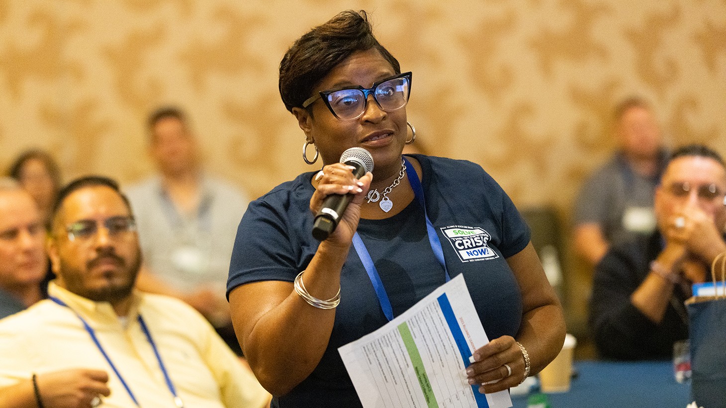 A Black woman, speaking into a handheld microphone at a conference