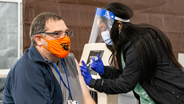 Masked women giving needle to masked man in left arm