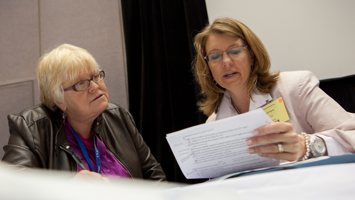 Alt text=” “Two women at a table, reviewing a document together 