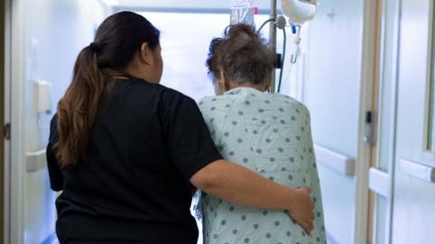 Nurse walking down a hospital corridor with elderly patient 