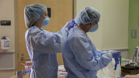 Two health care workers getting gowned up to perform surgery 