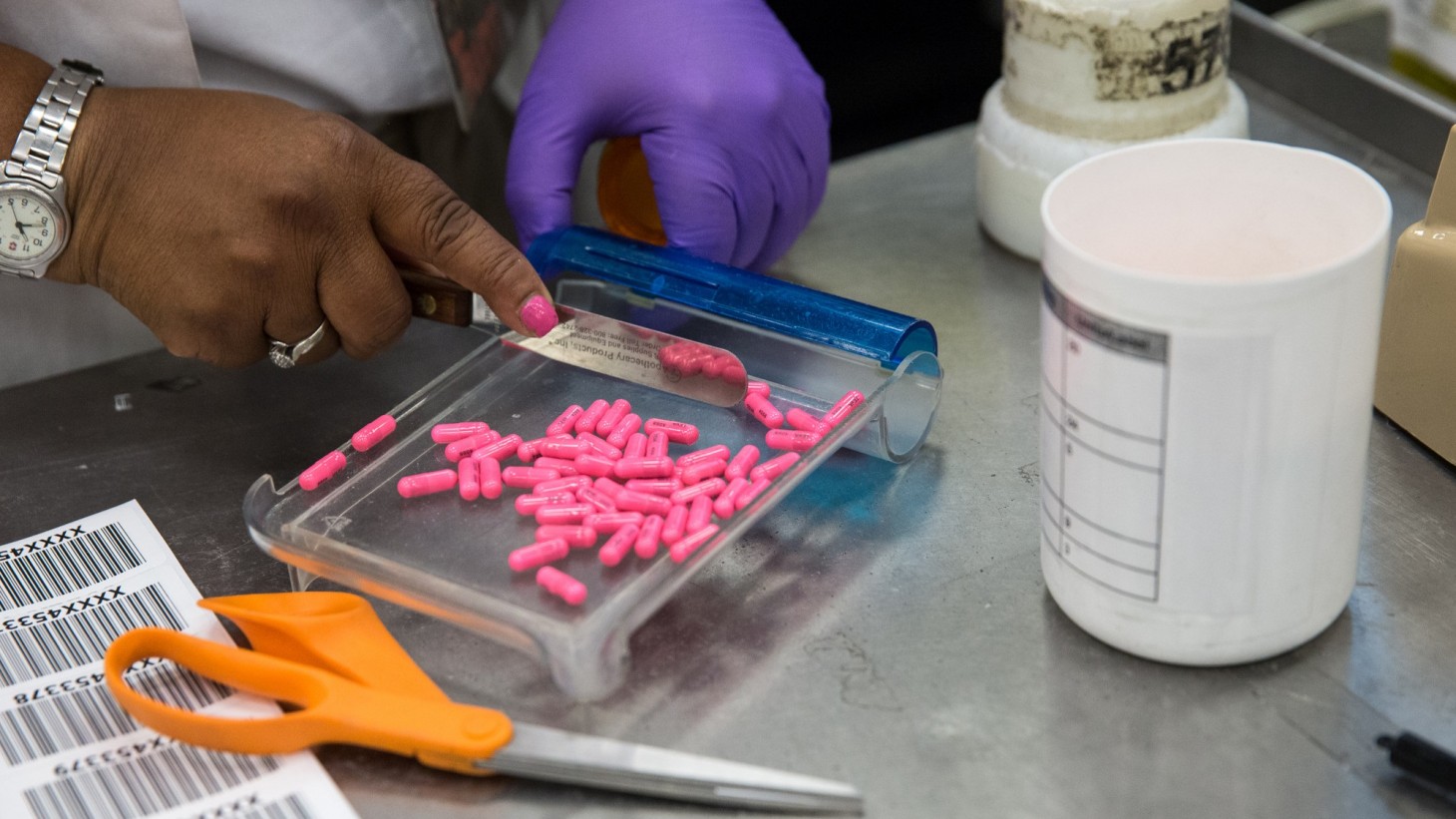 A pair of hands counting out pink pills in a clear tray 