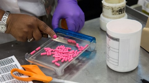 A pair of hands counting out pink pills in a clear tray 