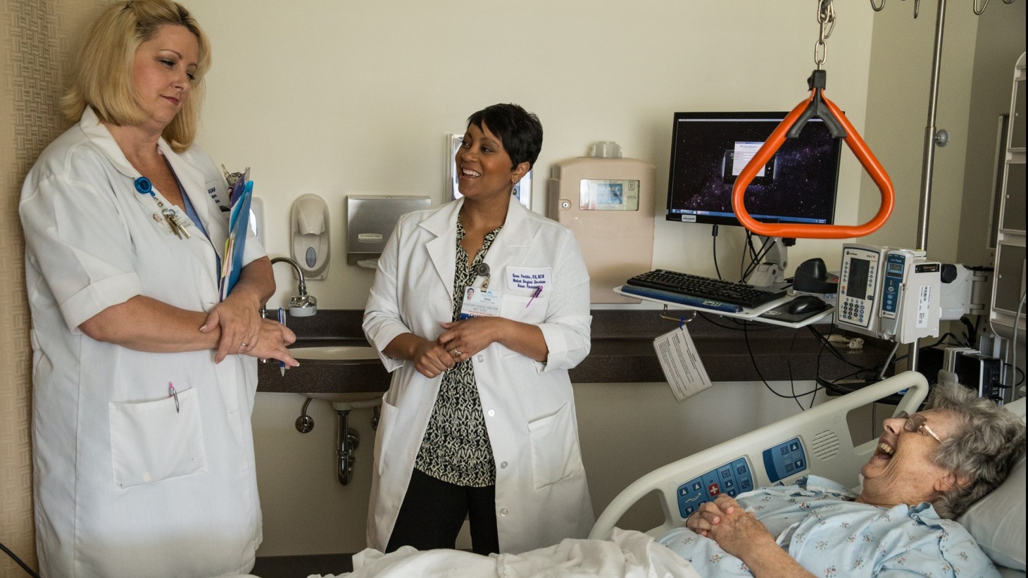 Two health care professionals in a hospital room with a patient 