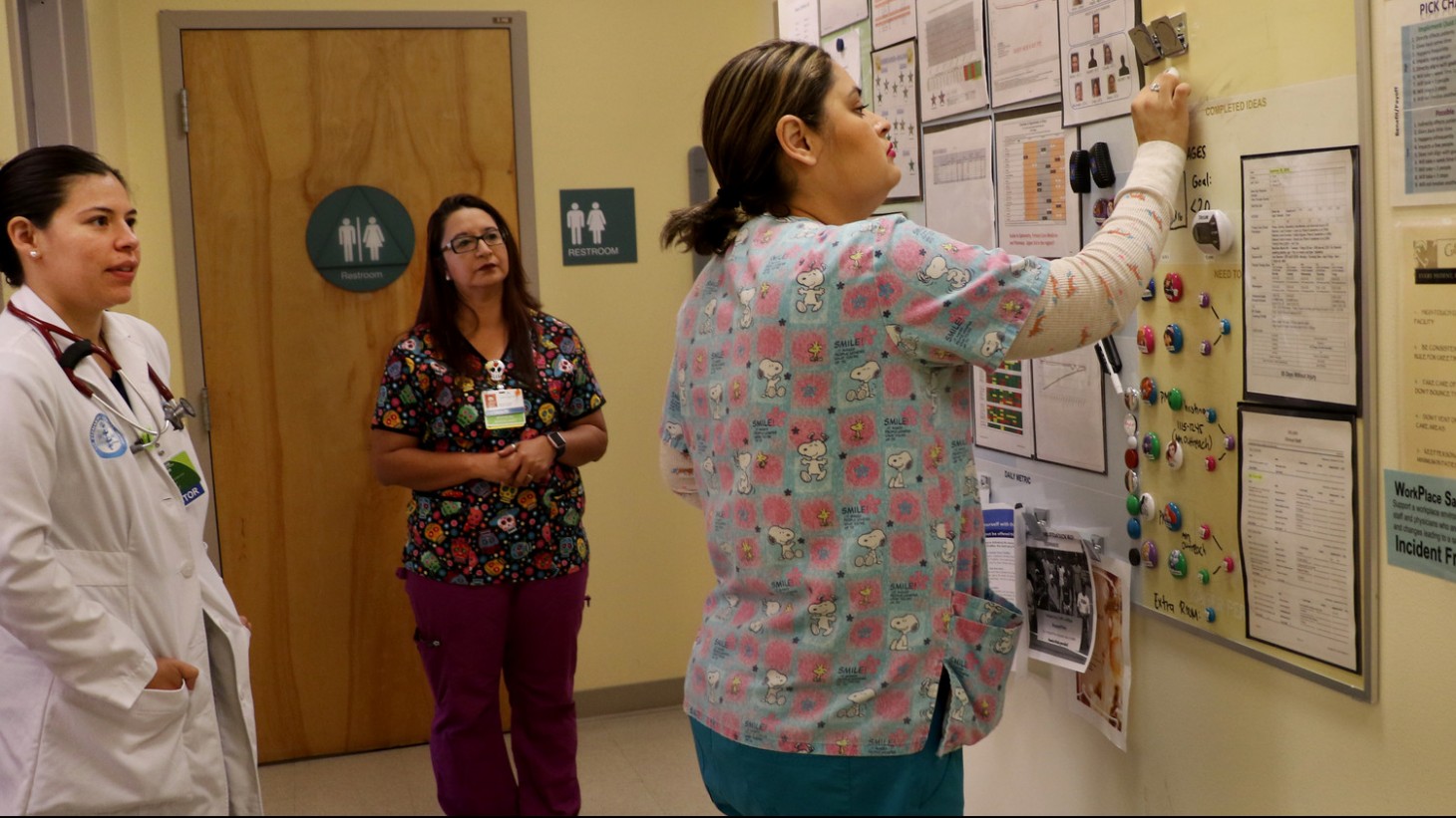 Health care workers filling in a huddle board in a clinic hallway 