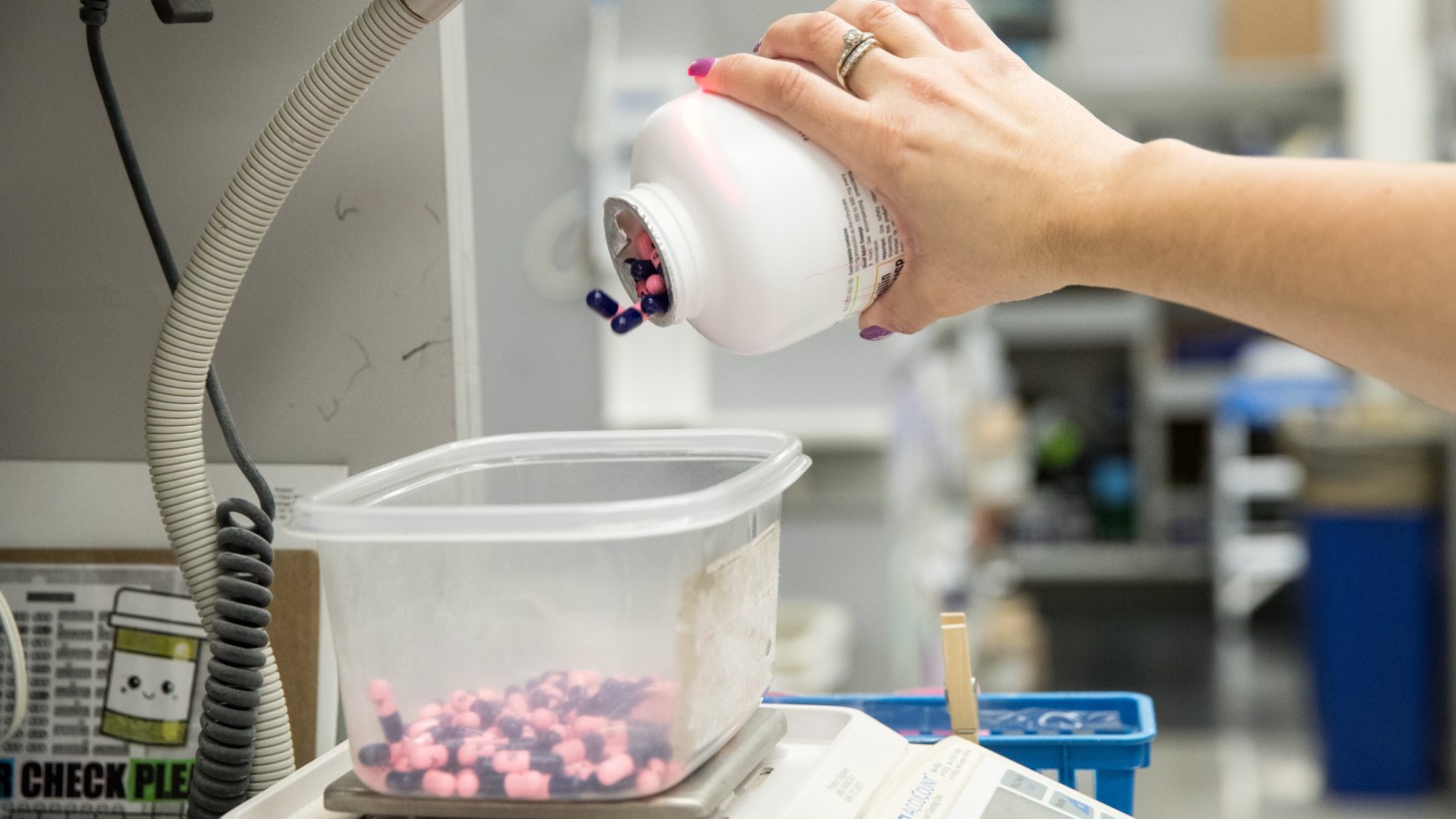 woman's hand pouring pink and brown capsules into a plastic bin 