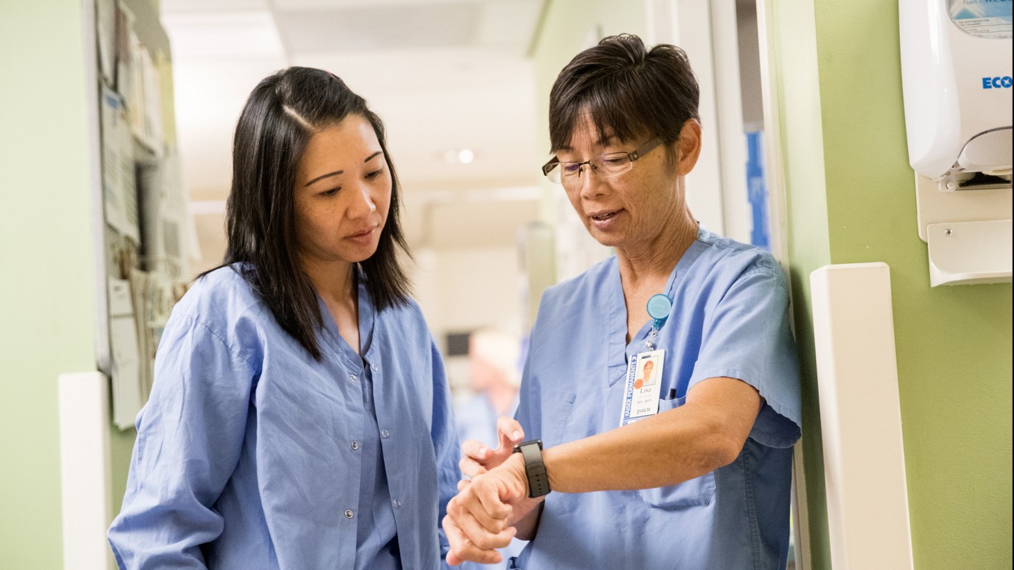 Two nurses, wearing blue scrubs, talking with each other