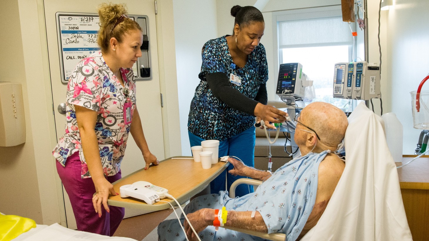 Two caregivers in a hospital room with an elderly patient 