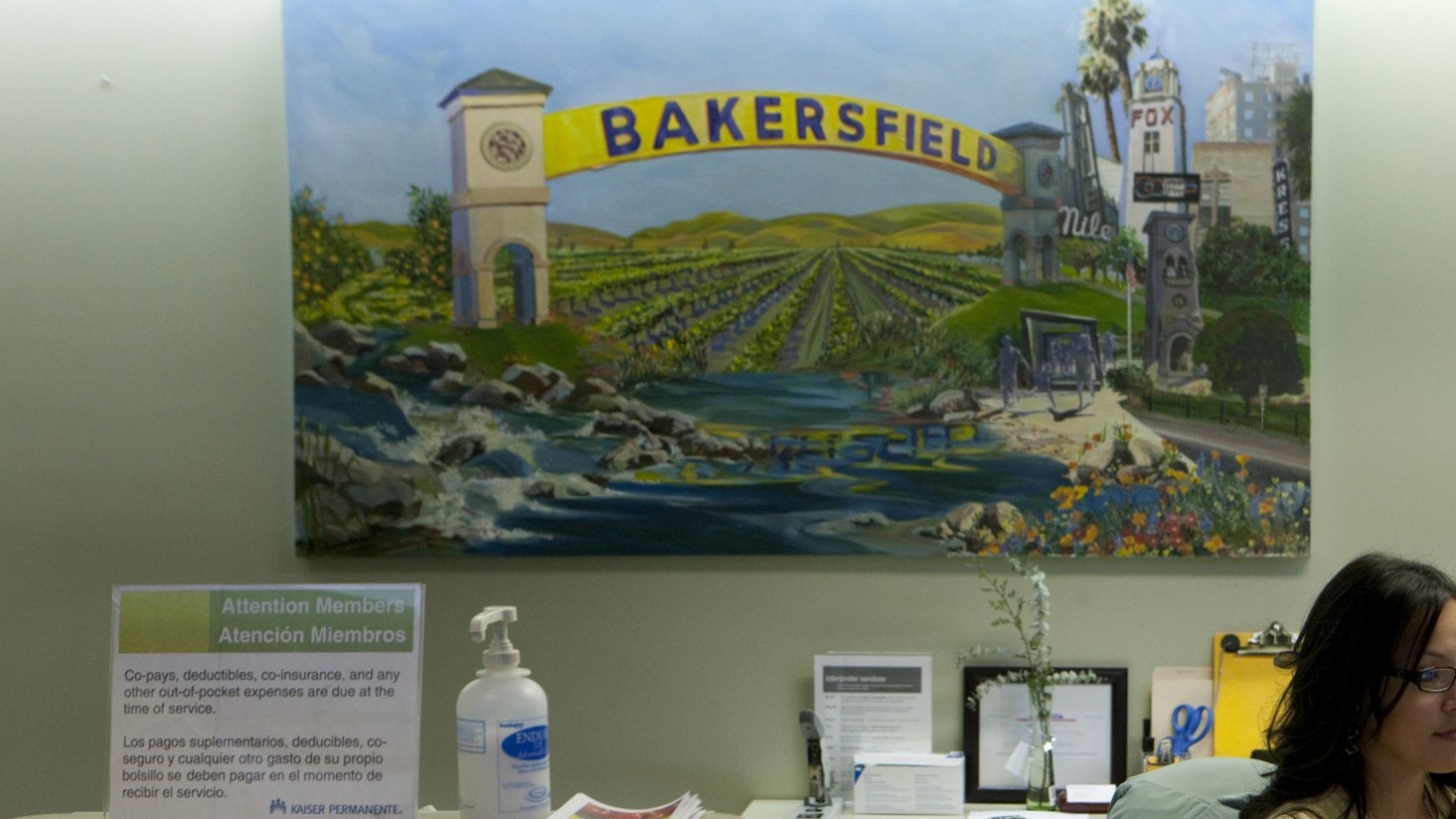 Receptionist at her desk under a painting of Bakersfield