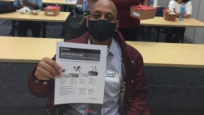 A black man, wearing a mask, holding up a flier