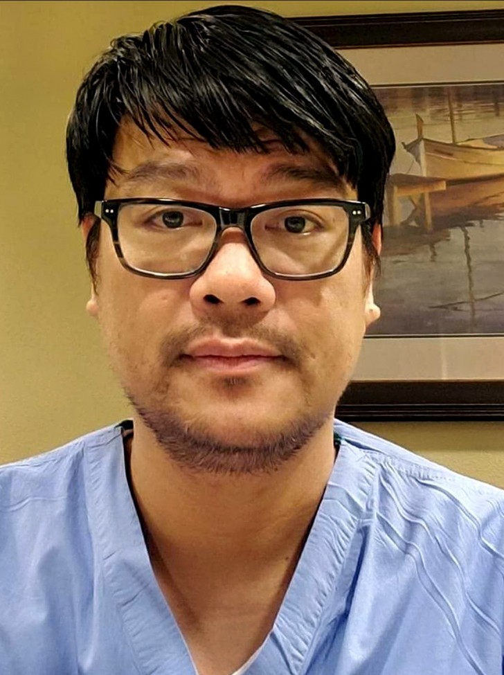 Asian male with black hair wearing glasses and blue scrubs